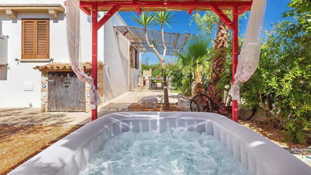 Uma banheira de hidromassagem sob uma pérgola de madeira, com um céu azul límpido ao fundo.