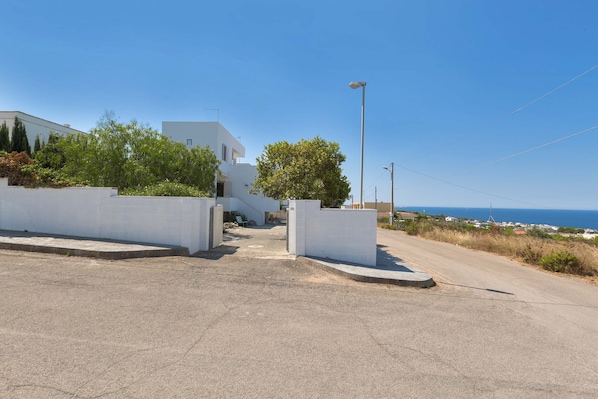 A residential street with white houses, a clear sky, and a view of the sea.