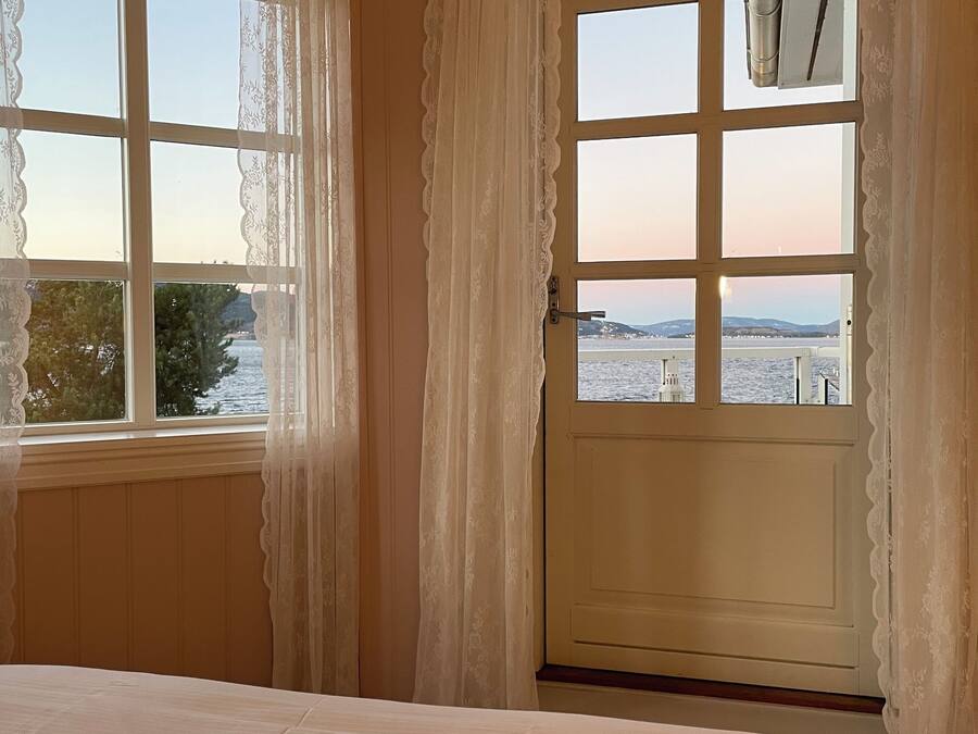 Quarto de hotel com cama, vista para um corpo de água e porta que dá para o exterior.