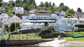 A coastal property with a large house featuring multiple balconies and a terrace with umbrellas.