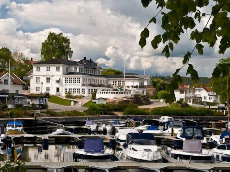 A marina with several boats docked, a large white building in the background, and a cloudy sky.