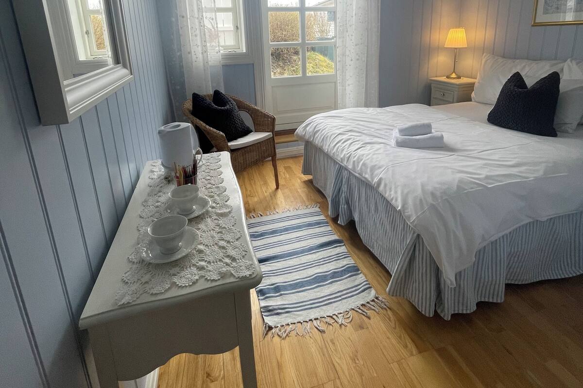 Un dormitorio con cama, mesita de noche y ventana con cortinas.