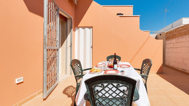 An outdoor dining area with a table set for two, chairs, a bottle of wine, and a plate of food. - 2038 Villetta Gloria (Alliste)
