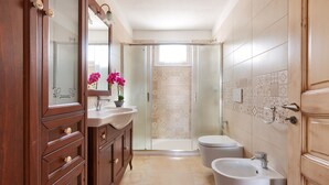 A bathroom with a wooden vanity, a sink, a toilet, and a shower area. - 2038 Villetta Gloria (Alliste)