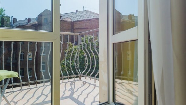 Blick von einem Balkon mit Metallgeländer, einem Stuhl und einem Gebäude im Hintergrund.