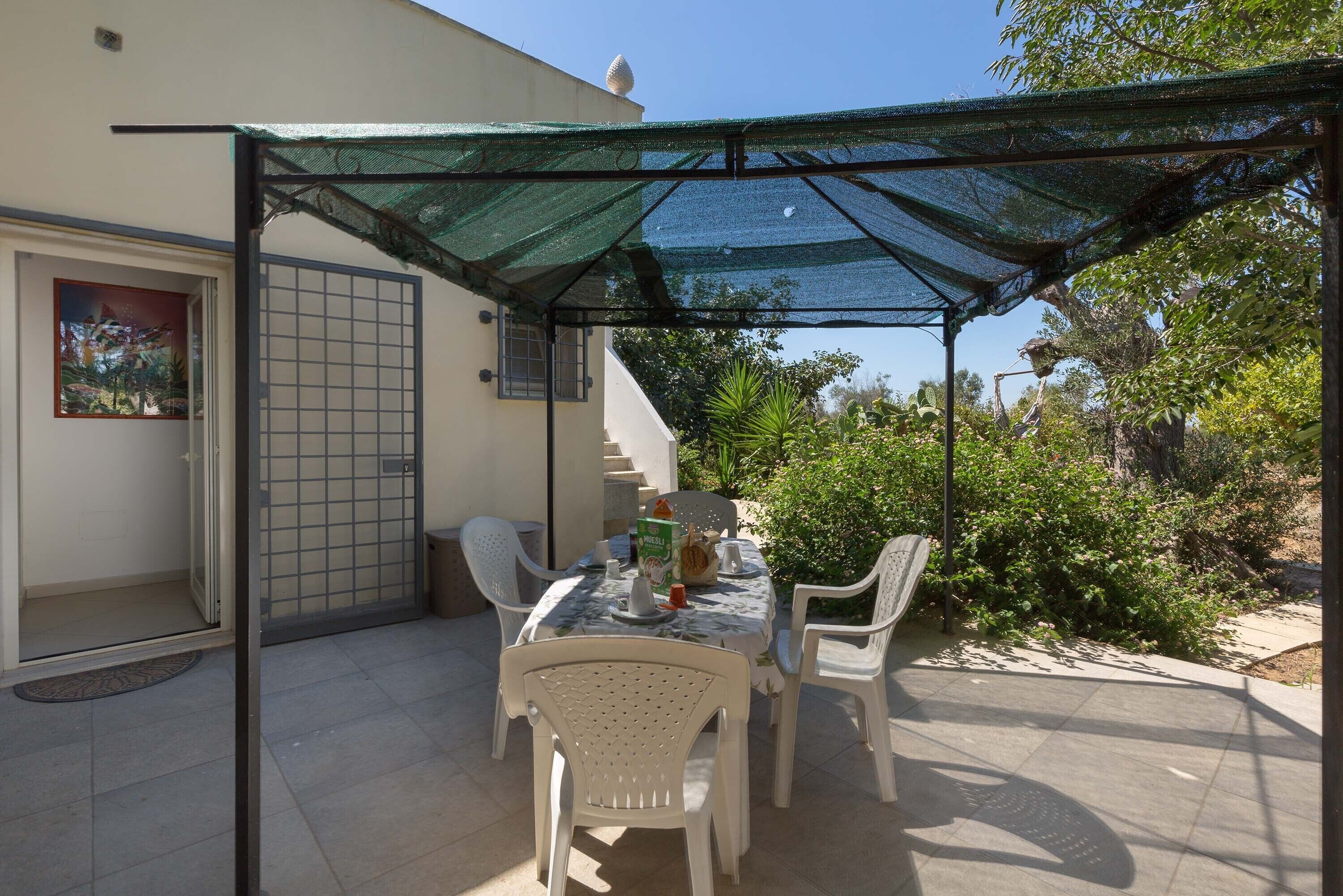 Eine Außenpatio mit Tisch und Stühlen, ein überdachter Bereich mit Netzdach und eine Tür mit Gittermuster.