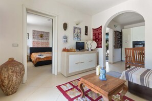 A room with a bed, a TV, a wooden table, and a large vase.