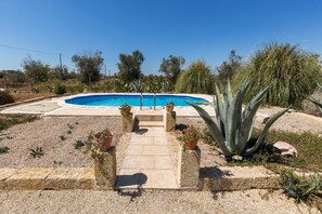 A swimming pool with a stone pathway leading to it, surrounded by various plants and trees. - 2090 La Terrazza del Salento (Matino)