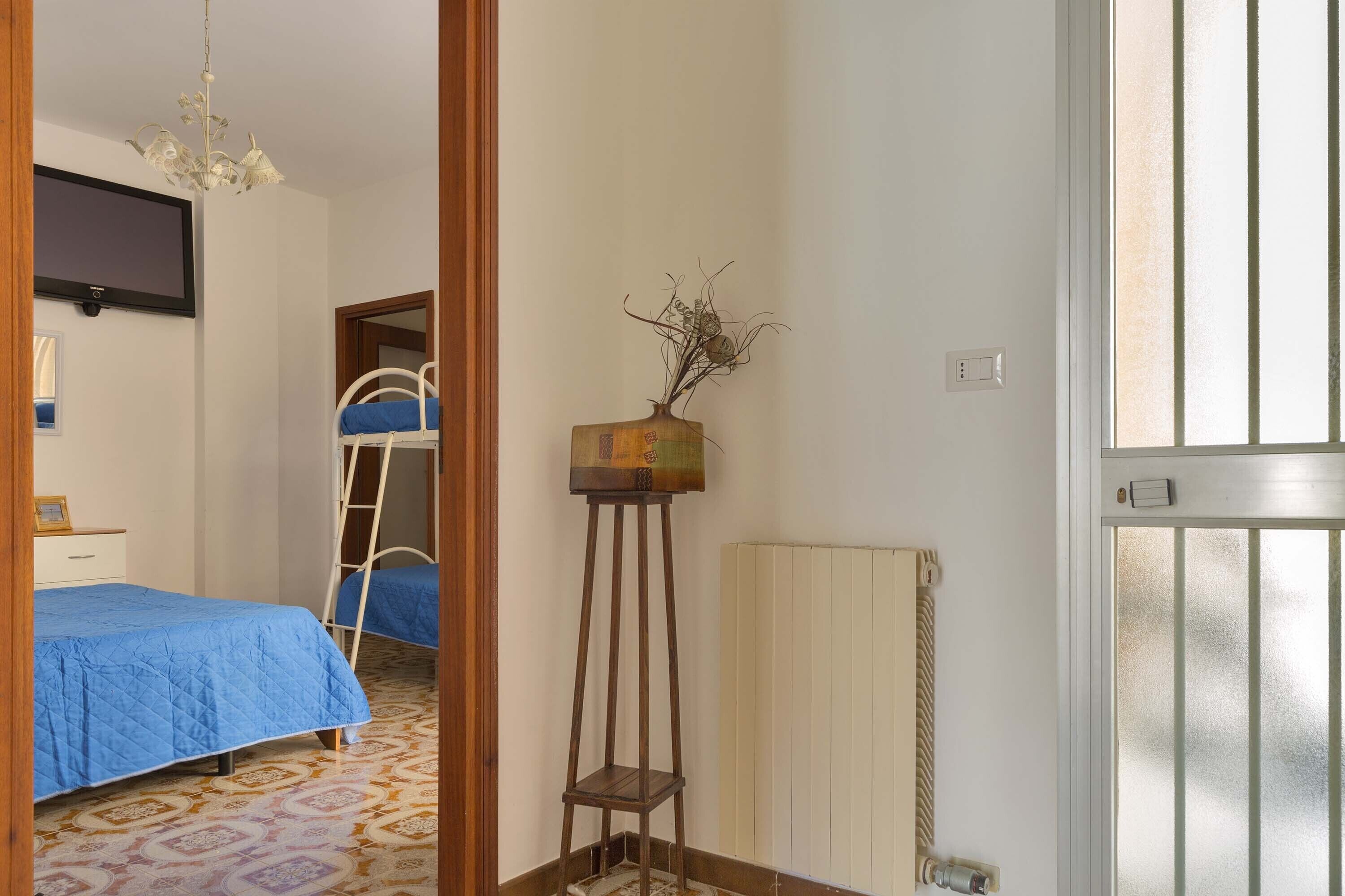 Een slaapkamer met een bed, een dressoir, een spiegel, een radiator en een deur met een geëtste ruit.