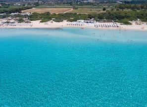 An aerial view of a beach with clear turquoise waters, a sandy shore, and several beach umbrellas and sun loungers.