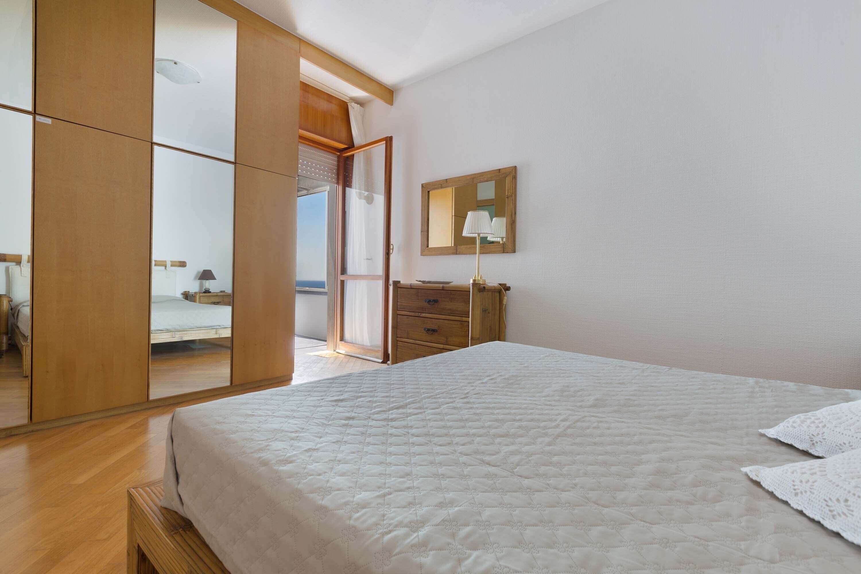 A bedroom with a large bed, wooden wardrobe, and a mirror on the wall.
