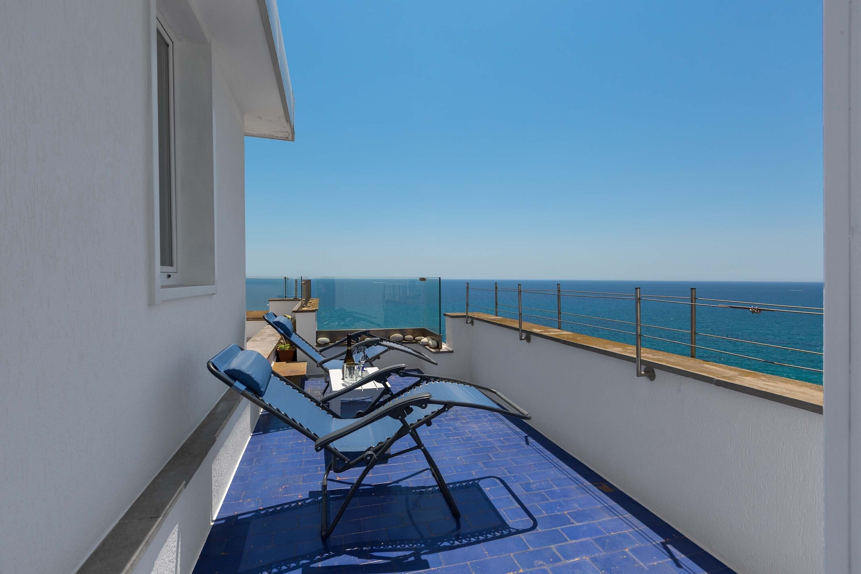 Ein Balkon mit Meerblick, ausgestattet mit zwei Liegestühlen und einem kleinen Tisch.