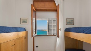 A compact room with bunk beds, a wooden wardrobe, and a window with a view of the sea. - 2016 Attico Bellavista (Gallipoli)