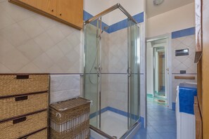 Ein Duschbereich mit Glastüren, Fliesenboden und einem Holzkabinet darüber.