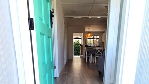Un couloir au plancher de bois mène à une salle à manger équipée d’une table et de chaises.