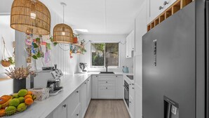 Une cuisine moderne avec des meubles blancs, un réfrigérateur gris, un four encastré et une fenêtre donnant sur un paysage verdoyant.