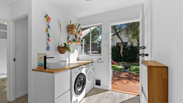 Une cuisine compacte équipée d’un lave-linge, d’un plan de travail en bois et d’une fenêtre donnant sur un jardin.
