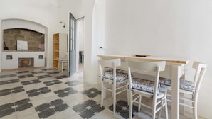 Un coin repas avec un sol à carreaux, des chaises blanches, une table en bois et une cheminée en pierre.