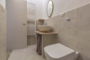 A bathroom with a white toilet, a beige sink with a bowl, and a towel hanging on a rack.
