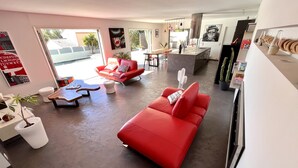 Ein modernes Wohnzimmer mit einem roten Sofa, einem Holztisch und einem weißen Pouf. Ein großes Fenster lässt natürliches Licht herein und bietet einen Ausblick nach draußen.
