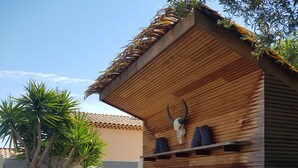 Ein Holzbau mit geneigtem Dach, einem aufgehängten Kuhschädel und einer Reihe von Liegestühlen mit Kissen.