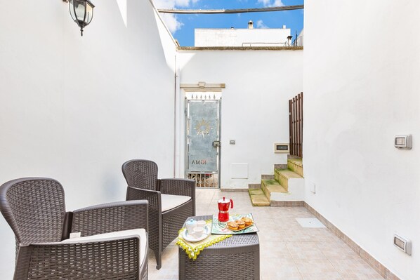 A patio with wicker furniture and a table set with a coffee pot, cups, and pastries.