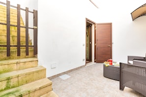 A clean, tiled patio area with a wooden door, a wicker sofa, and a small table with items on it.