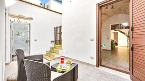 Un patio con muebles de mimbre, una mesa con un plato de comida y una puerta que da a un espacio interior con una escalera.