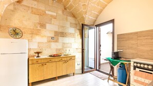 Una cocina con pared de piedra, armarios de madera, un refrigerador blanco, una estufa y una mesa verde.