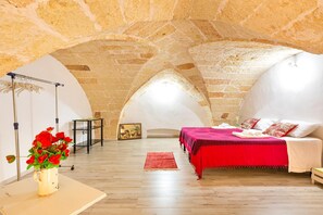 A bedroom with a stone ceiling, a bed with a red bedspread, and a vase of red flowers on a table. - 2192 Casetta di Adriana (Copertino)