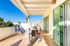 A balcony with a table and chairs, a green door, and a view of the sky.