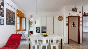 Uma sala de jantar com uma mesa e cadeiras brancas, um sofá vermelho e uma cozinha com armários e fogão.