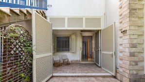 Um pátio com piso de azulejos, duas cadeiras, um portão e um muro com decoração em treliça.