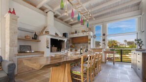 A spacious kitchen with a large wooden island, a stone fireplace, and a view of the outdoors through large windows. - Villa Padangi (Gallipoli)