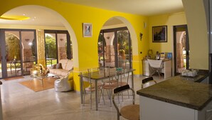 A spacious living area with a glass dining table, comfortable seating, and large windows offering views of the outdoors. - 2099 Villa Arkè (Alliste)