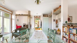 A dining area with a glass table, green chairs, a white table runner, and a bookshelf filled with books. - 2143 Villa Corsarina (Nardò)