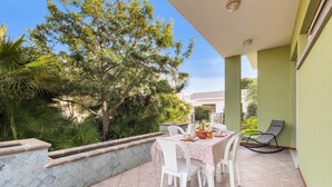 An outdoor patio with a table set for dining, surrounded by greenery and a view of a building in the background. - 2143 Villa Corsarina (Nardò)