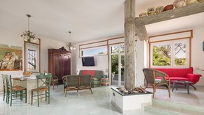 A spacious living area with a dining table, chairs, a red sofa, wicker chairs, a television, and a large window with a view of greenery. - 2143 Villa Corsarina (Nardò)