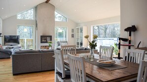 A spacious living room with a wooden dining table, white chairs, a grey sofa, and a TV. - Stunning home in Sölvesborg with WiFi (Sölvesborg)