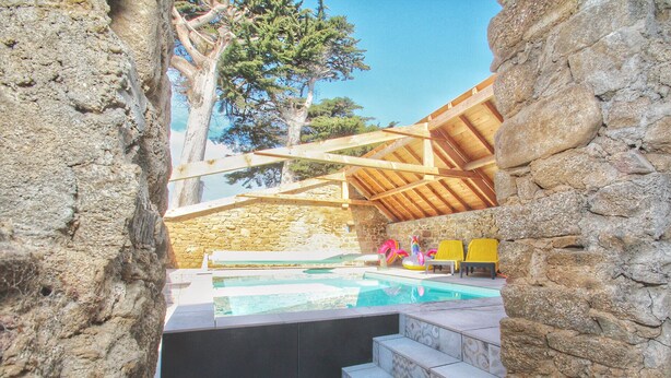 Un espace piscine agrémenté de murs en pierre, de poutres en bois et d’un escalier menant à la piscine.