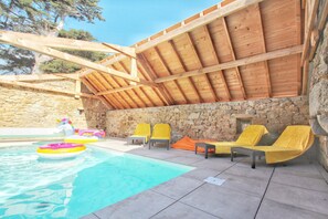 Un espace piscine agrémenté d’un mur en pierre, de poutres en bois et de chaises longues jaunes.