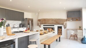 Une cuisine moderne dotée d’un four encastré, d’un coin repas avec un banc en bois et d’une cheminée en pierre.