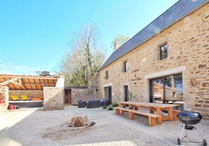 Un bâtiment en pierre doté d’une terrasse en bois, d’un espace extérieur aménagé pour s’asseoir et d’un barbecue.