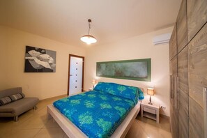 A bedroom with a bed, a nightstand, a lamp, a sofa, and a door.