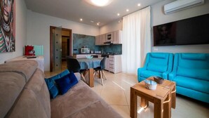 Un espacio habitable compacto con kitchenette, comedor y zona de estar con sofá y un sofá azul.