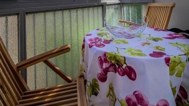 Un balcón con una mesa para dos, sillas de madera y vistas a montañas y cielo a través de amplias ventanas.