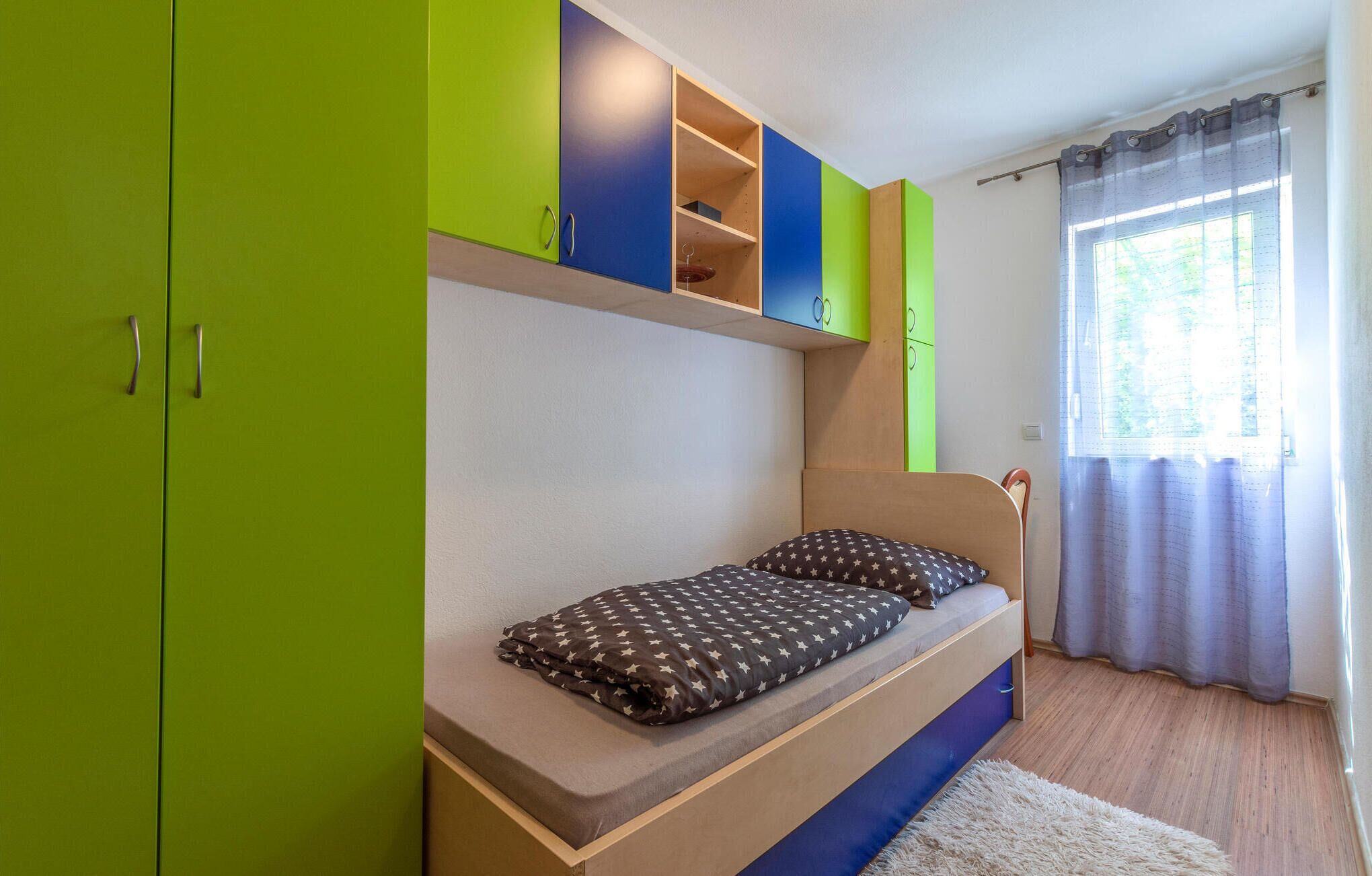 Ein Schlafzimmer mit einem Bett, grünen und blauen Schränken sowie einem Fenster mit Vorhängen.