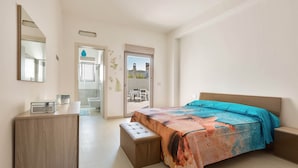 A bedroom with a bed, a bedside table, a nightstand, a dresser, and a mirror. There is a door leading to a balcony. - 2103 Villetta Clara (Nardò)
