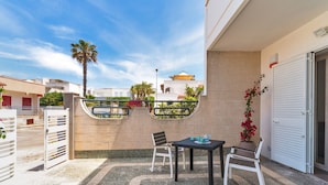 A terrace with a table and chairs, a palm tree, and a view of neighboring buildings. - 2103 Villetta Clara (Nardò)