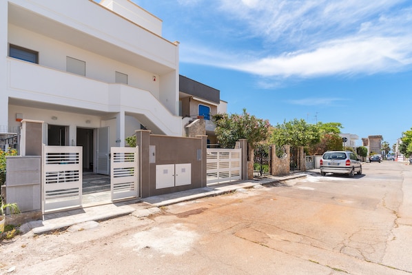 A modern residential building with a gated entrance, a staircase, and a car parked on the street.